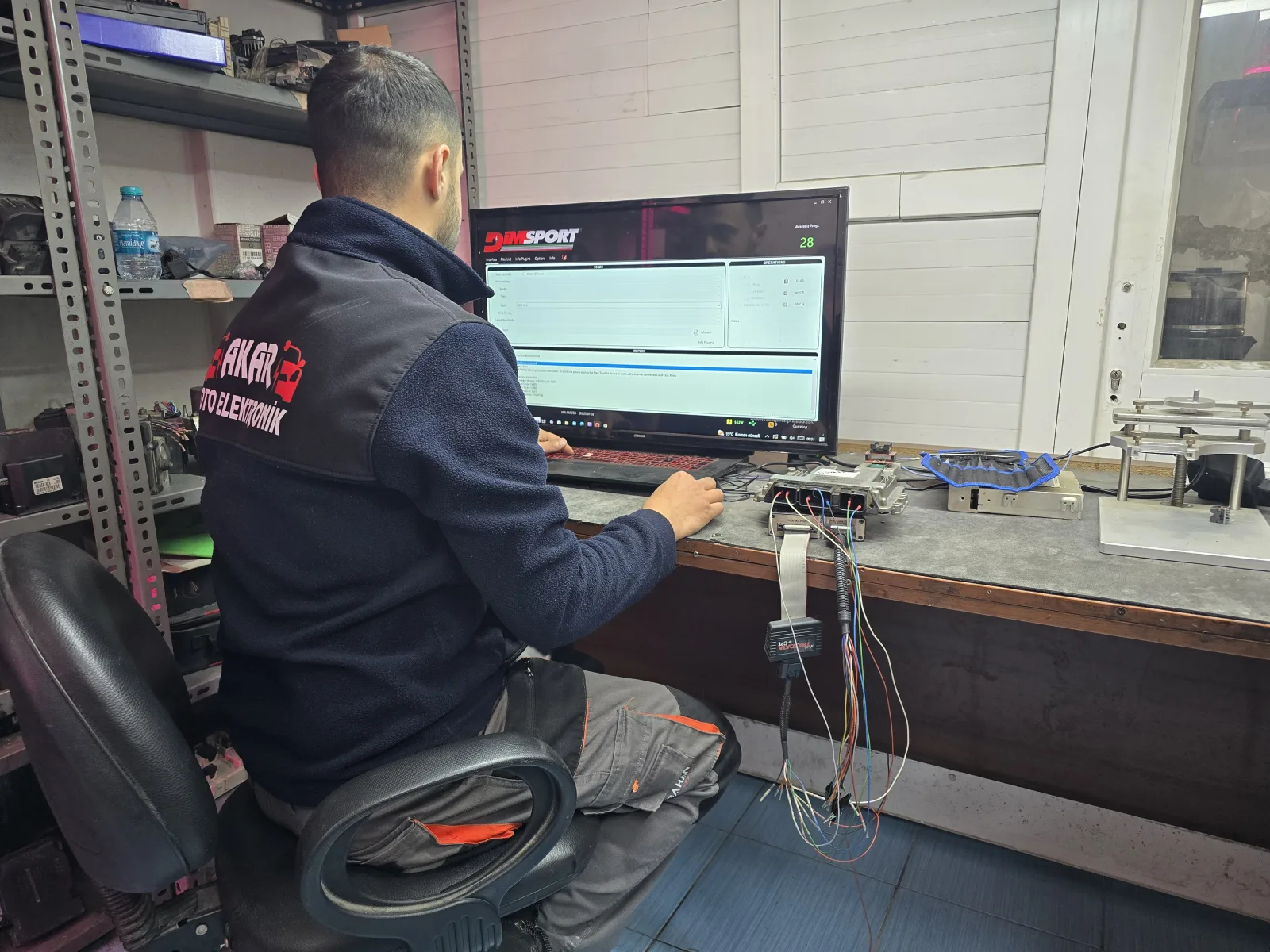 Akar Oto Elektronik iş kıyafetiyle bir teknisyen, ekrandaki yazılım üzerinden bağlı ünitede çalışıyor