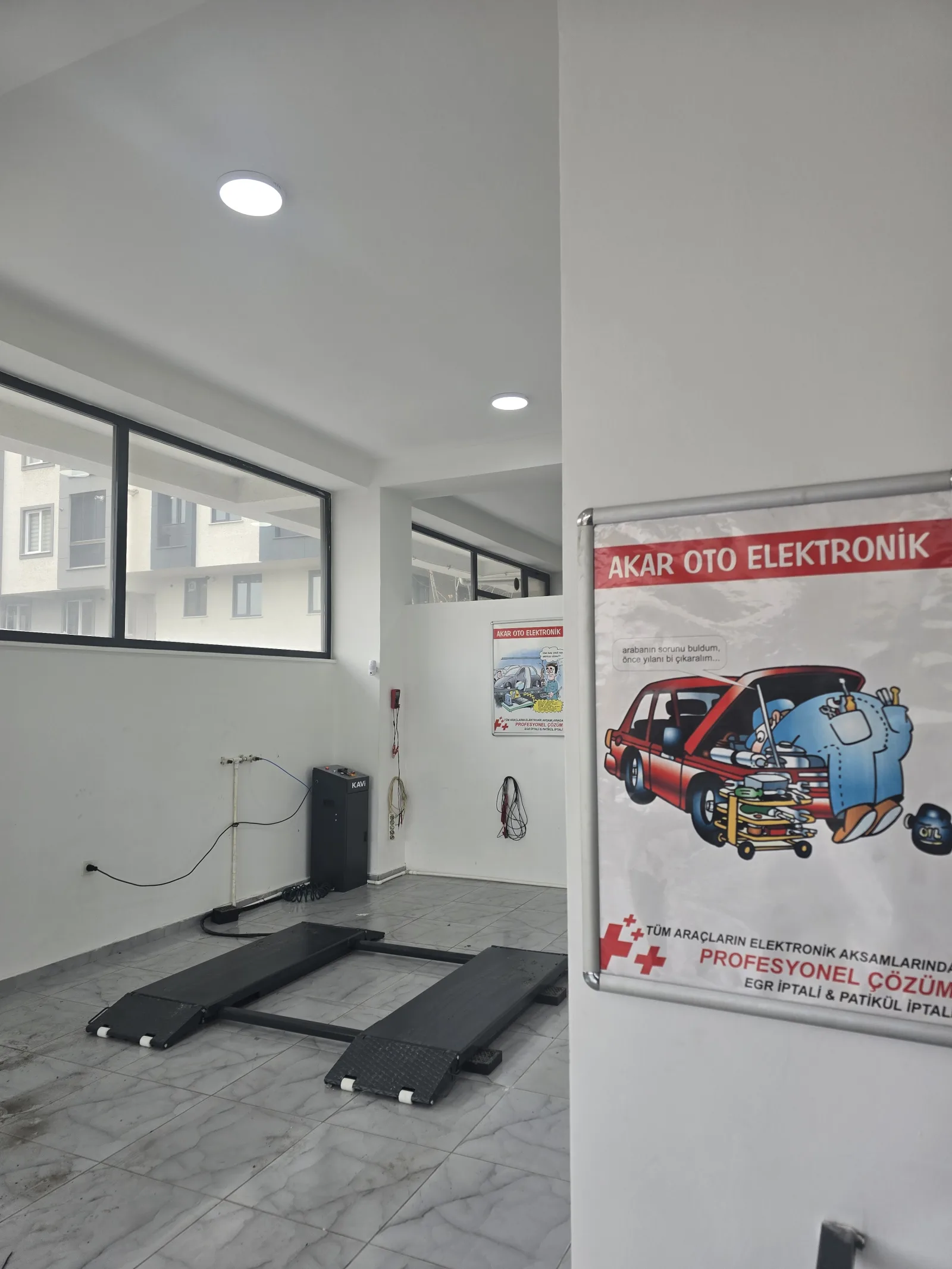 Duvarda asılı Akar Oto Elektronik bilgilendirme afişi ve atölye iç mekânı